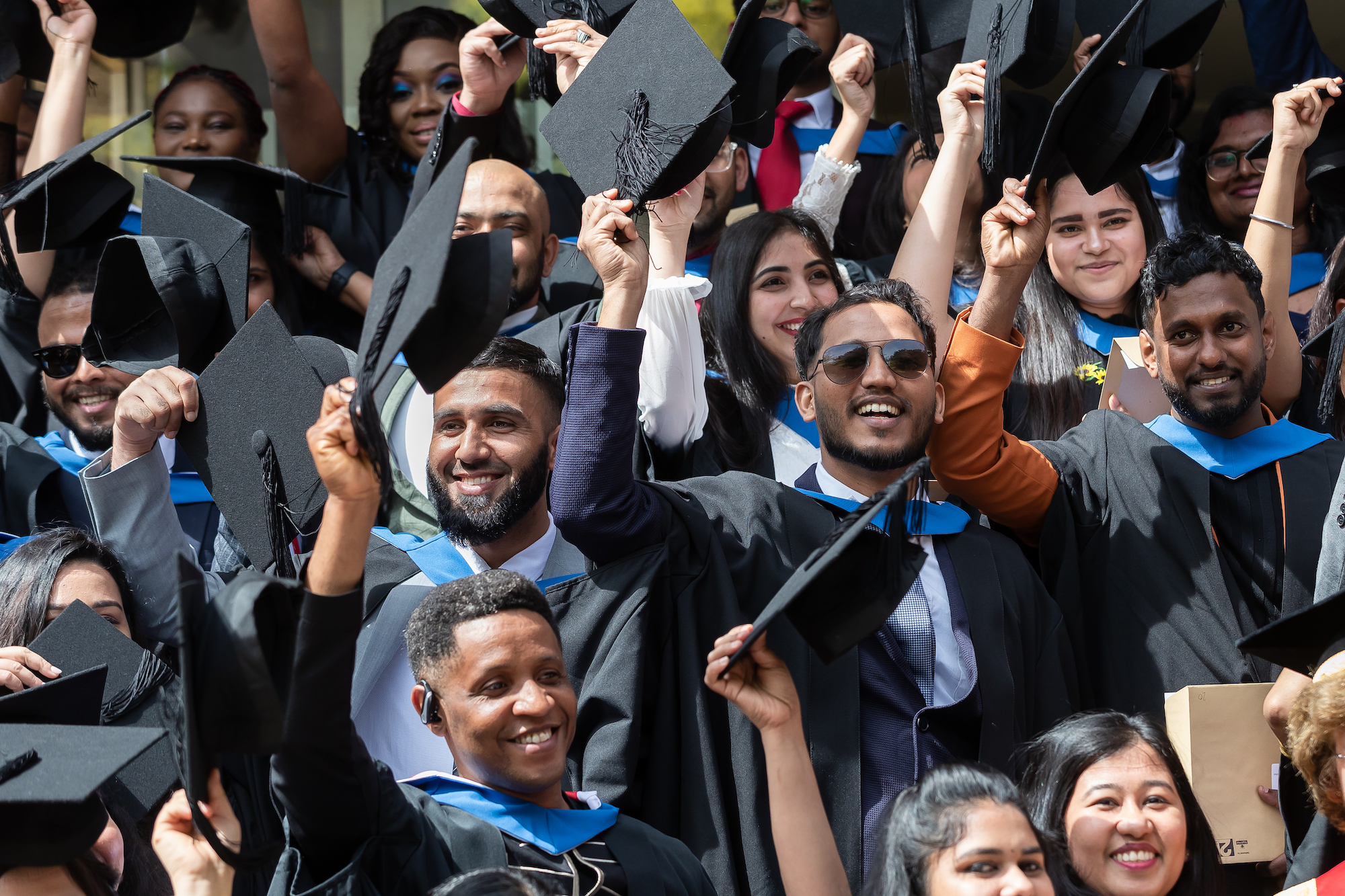 A group of International students graduating, wearing caps and gowns smiling at each other and the camera