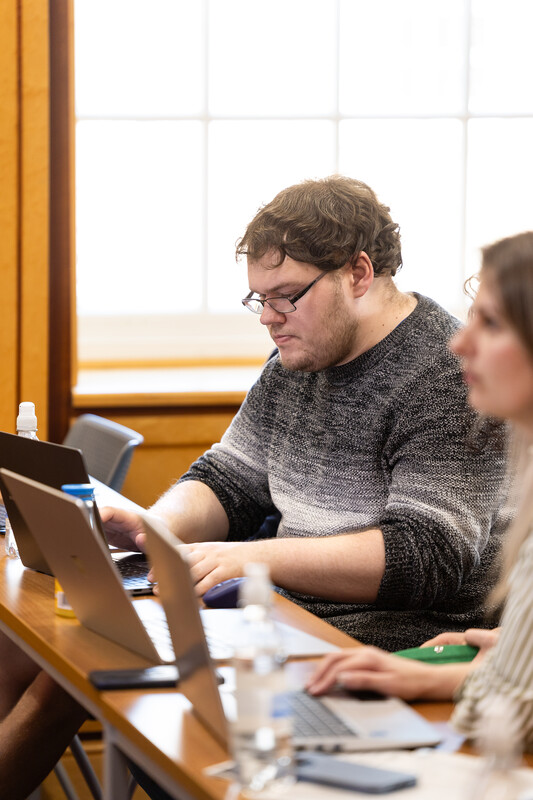 A research degree student on a laptop while sitting at a table, engaged in his task.