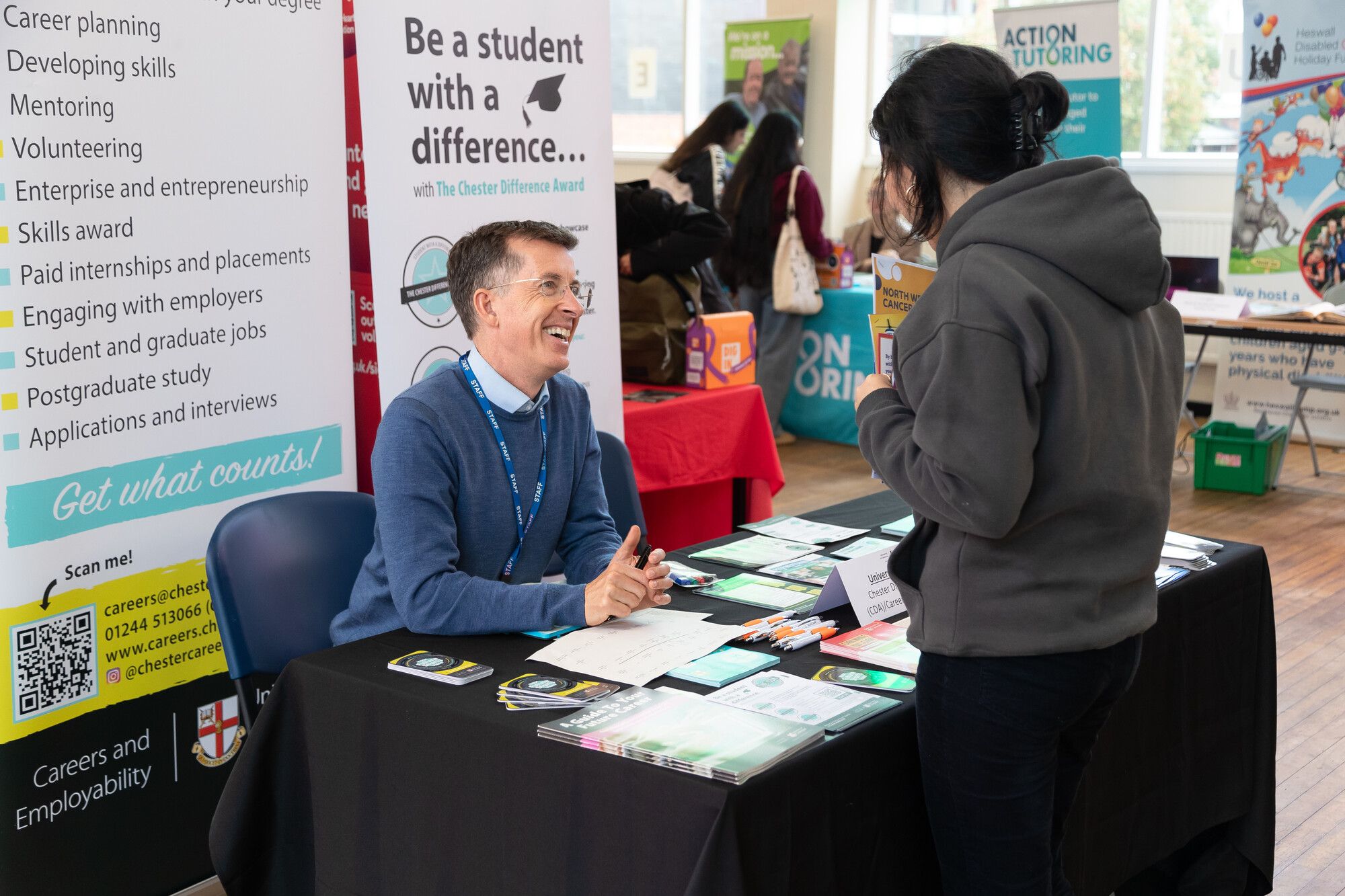 University careers and employability fair with a student discussing volunteering and skill development opportunities at an information stall featuring brochures and banners.