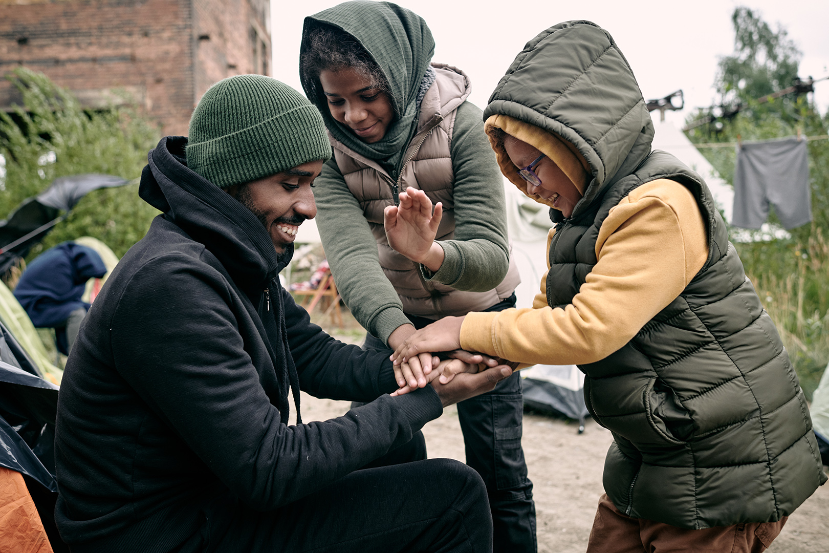A man and two children in warm hooded jackets smile as they stack their hands together outdoors