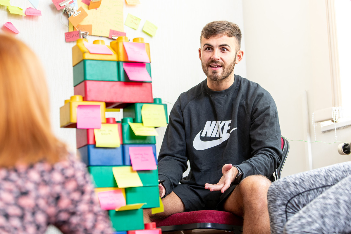 a man sitting on a chair facing a colourful tower of building blocks in front of him