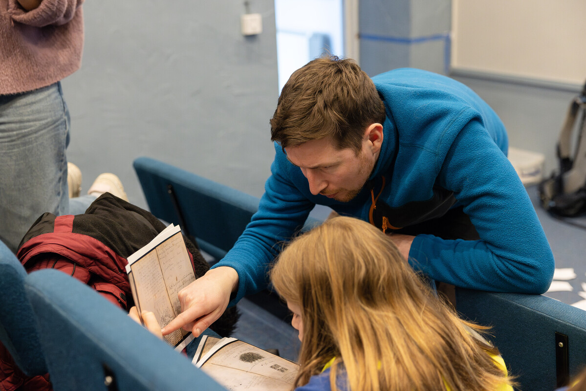 A man and two young girls sit on a bench, engaged in reading a book together, fostering a love for learning.