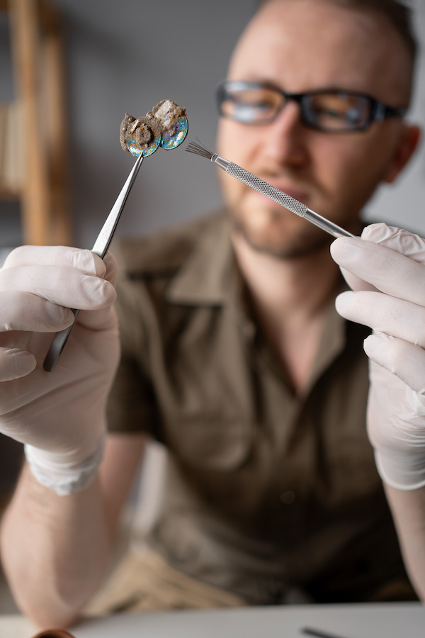 Archaeologist looking at an artefact, held with tweezers and a small brush