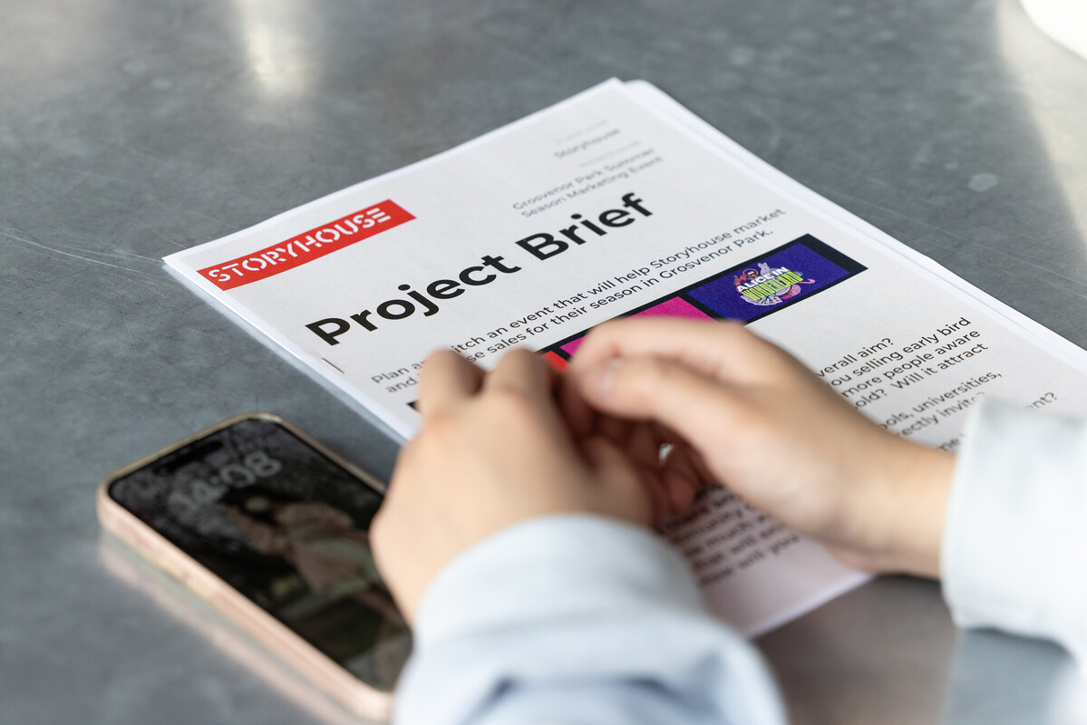Project brief document on a table with close up of hands and a phone