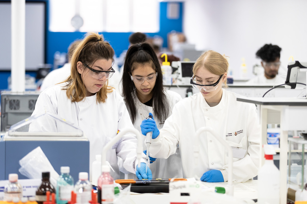 A group of students working in a laboratory, dressed in white coats standing next to tables.