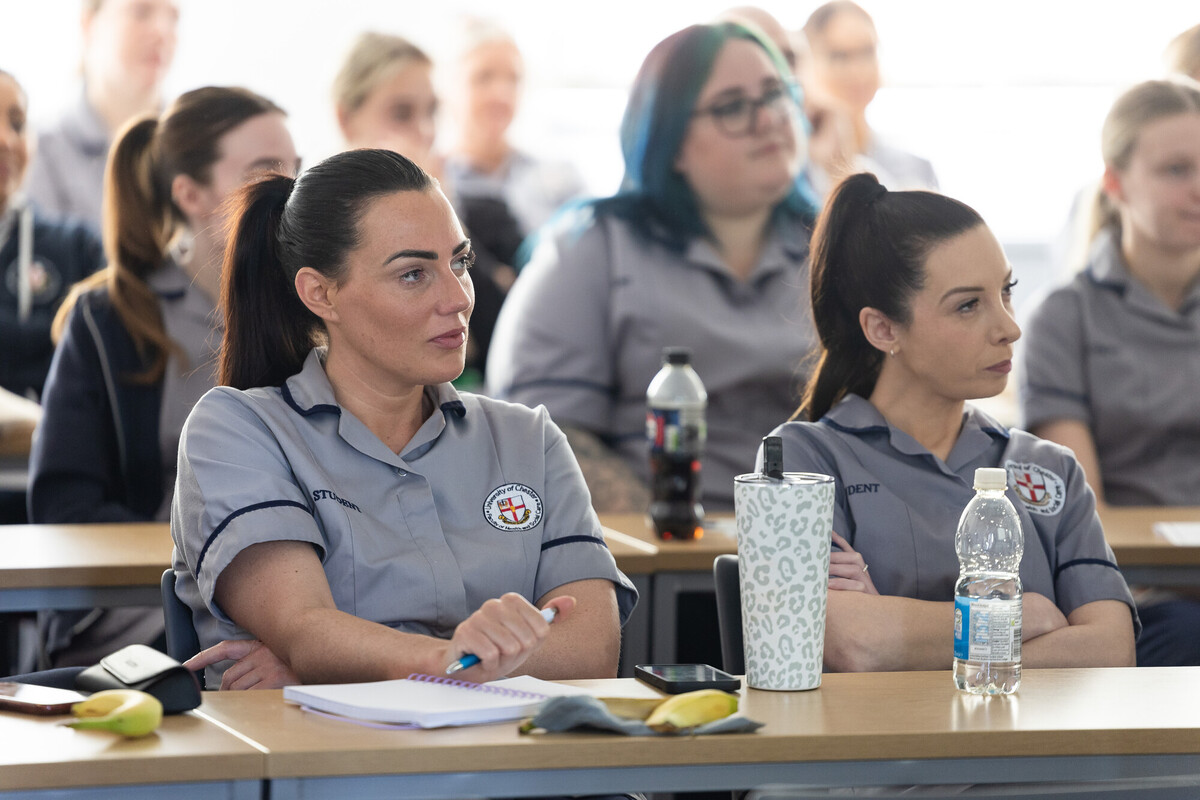 Student Nurses are seated at desks in a classroom setting, attentively listening to a seminar.