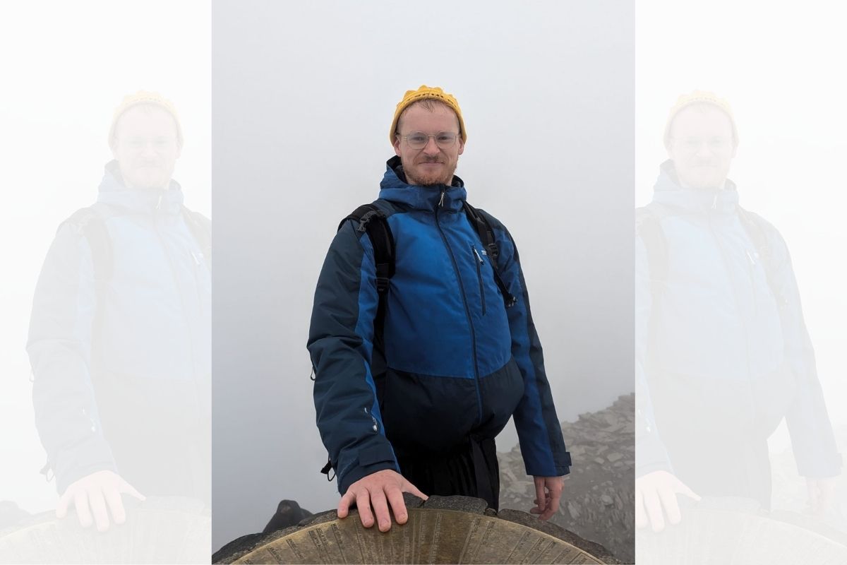 A man in a coat on the side of a mountain on a grey day - the background is obscured by cloud and fog.