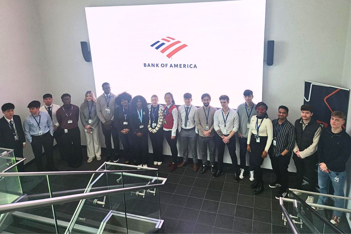 The camera looking down on a group of students lined up in a row between two staircases. In the background, a big screen with a Bank of America logo is on display.