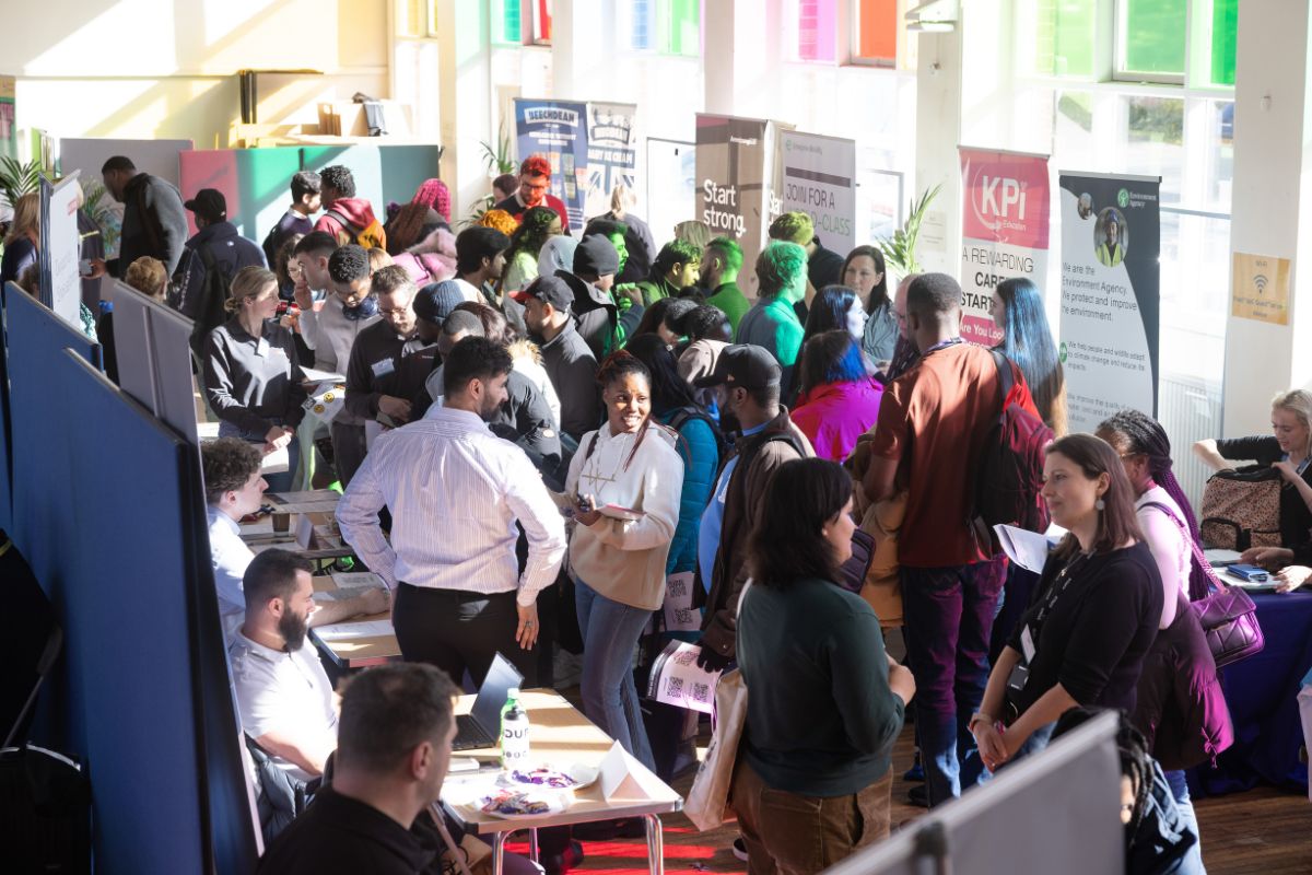 A group of people in a packed room looking at information stalls and discussing.