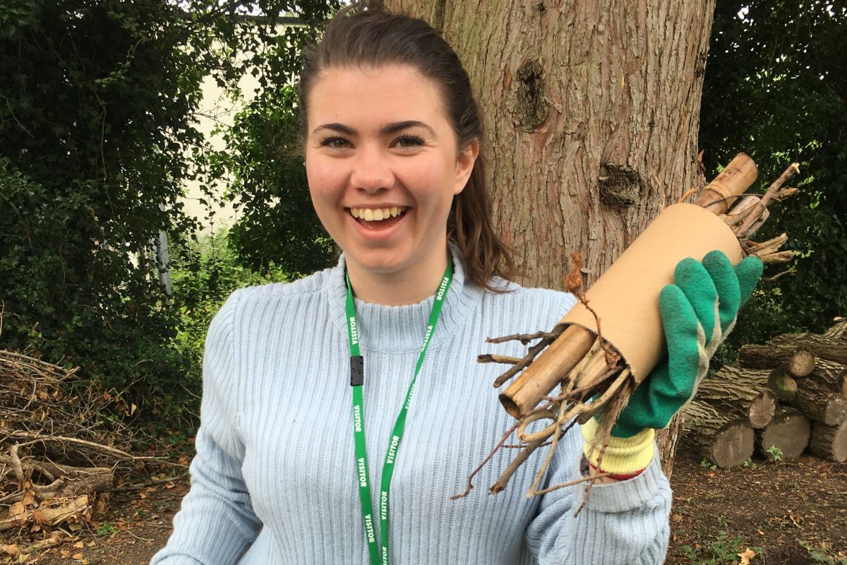 A student taking part in a conservation event, smiling, holding up a collection of branches and twigs.