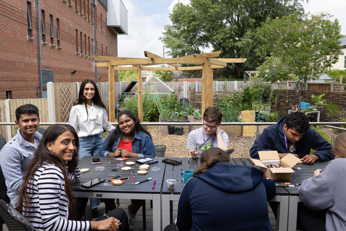 A group of people working on crafts at a table in the community garden. Several people are looking at the camera smiling.