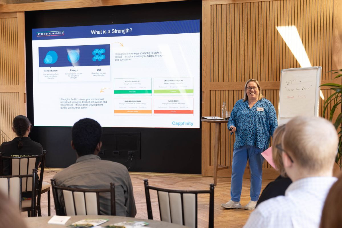 A woman giving a presentation in front of a screen describing what a Strengths Profile is.