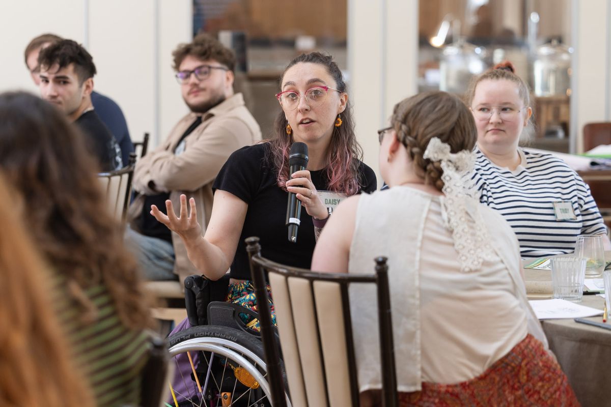 A young woman at a table holding a microphone asking a question