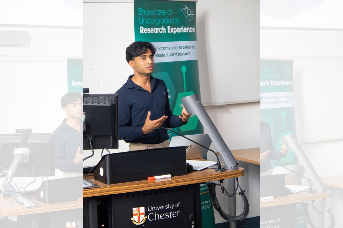 Aadhi standing at a lectern, giving a talk to an audience out of frame, at the Showcase of Undergraduate Research Experience, or SURE for short.