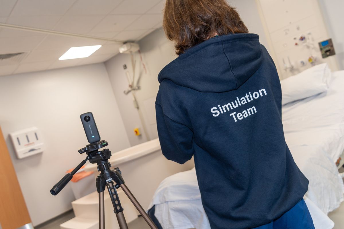An angled shot of the back of a person wearing a hoodie with 'Simulation Team' written on it, looking at a camera on a tripod