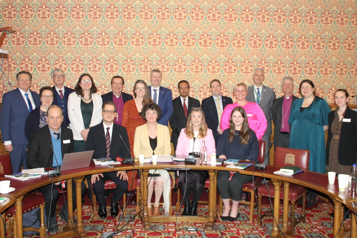 A group of people in a Houses of Parliament meeting room, all looking at the camera