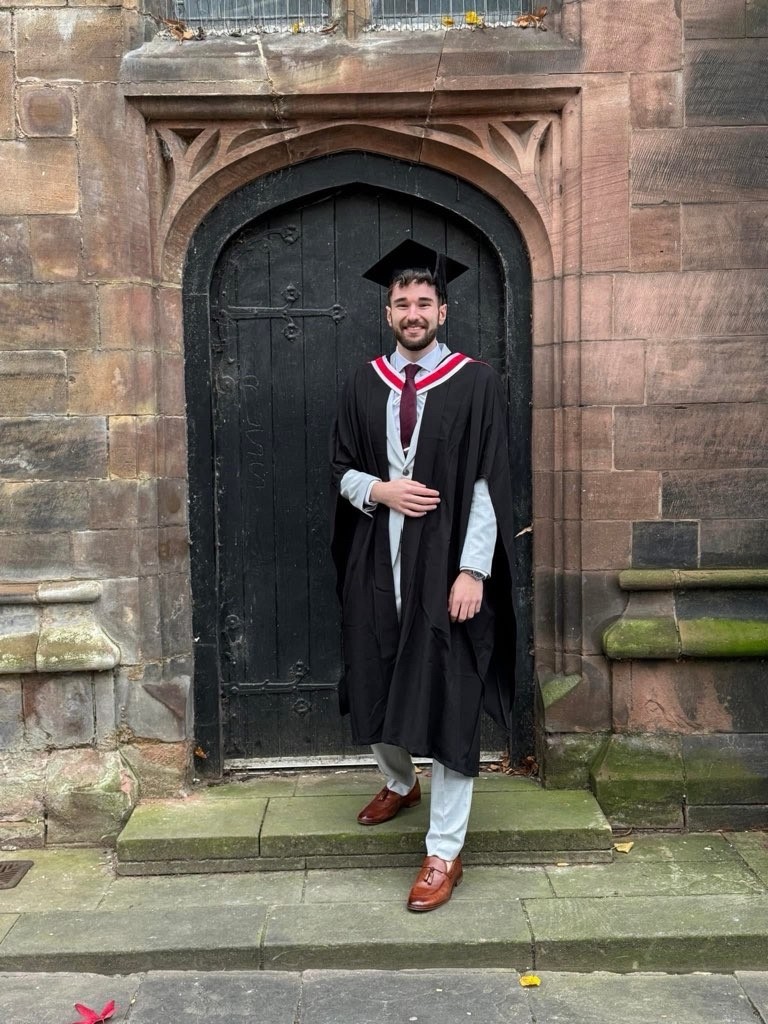 Student in graduate robes outside of doorway