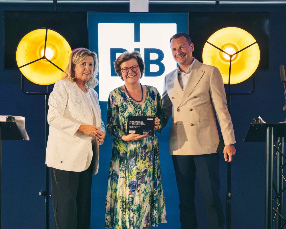 Vice-Chancellor Prof Eunice Simmons smiling while looking at the camera, holding an award. Also present is awards host Lucy Meacock.