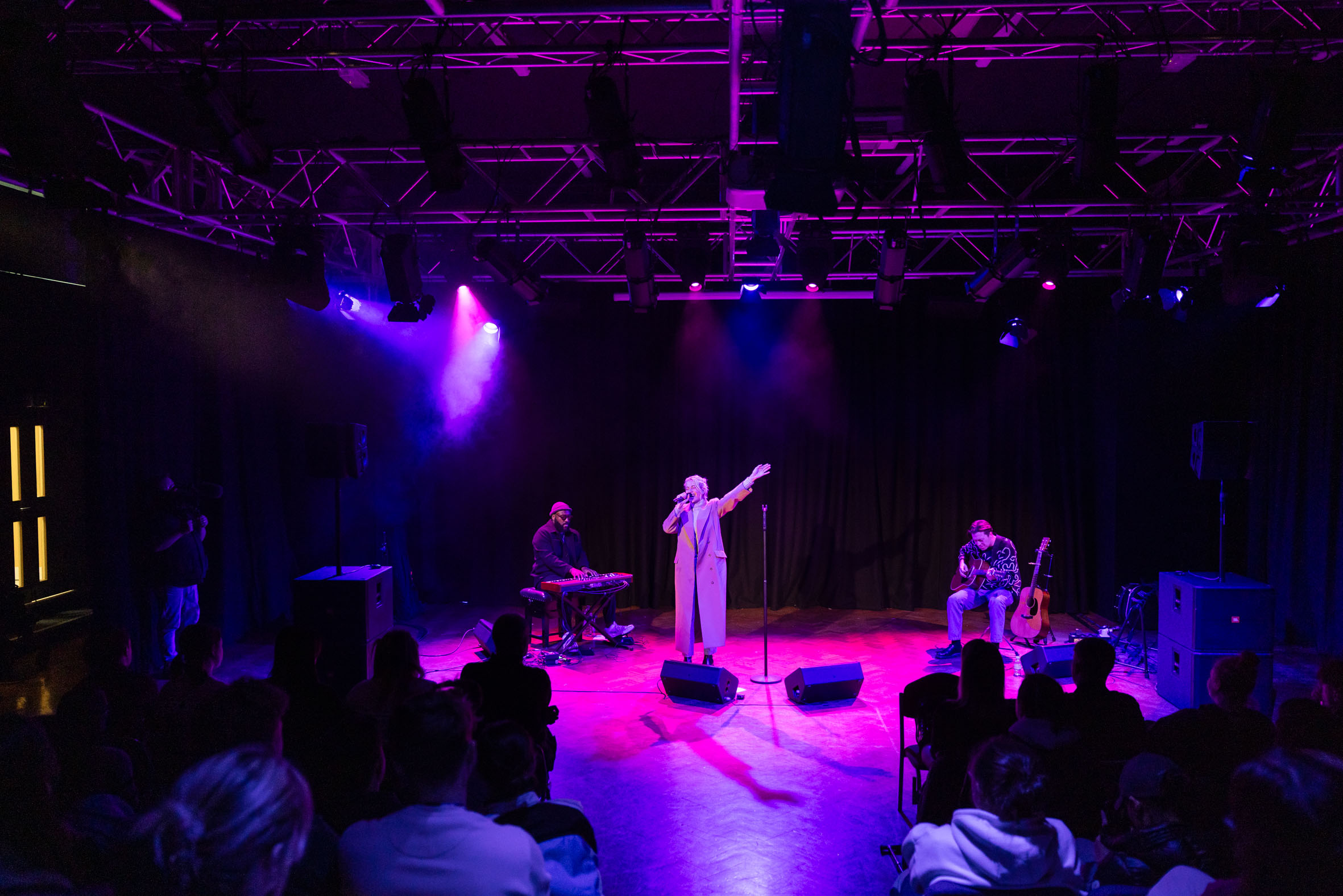 Pixie Lott standing and singing as she performs to students sat down.