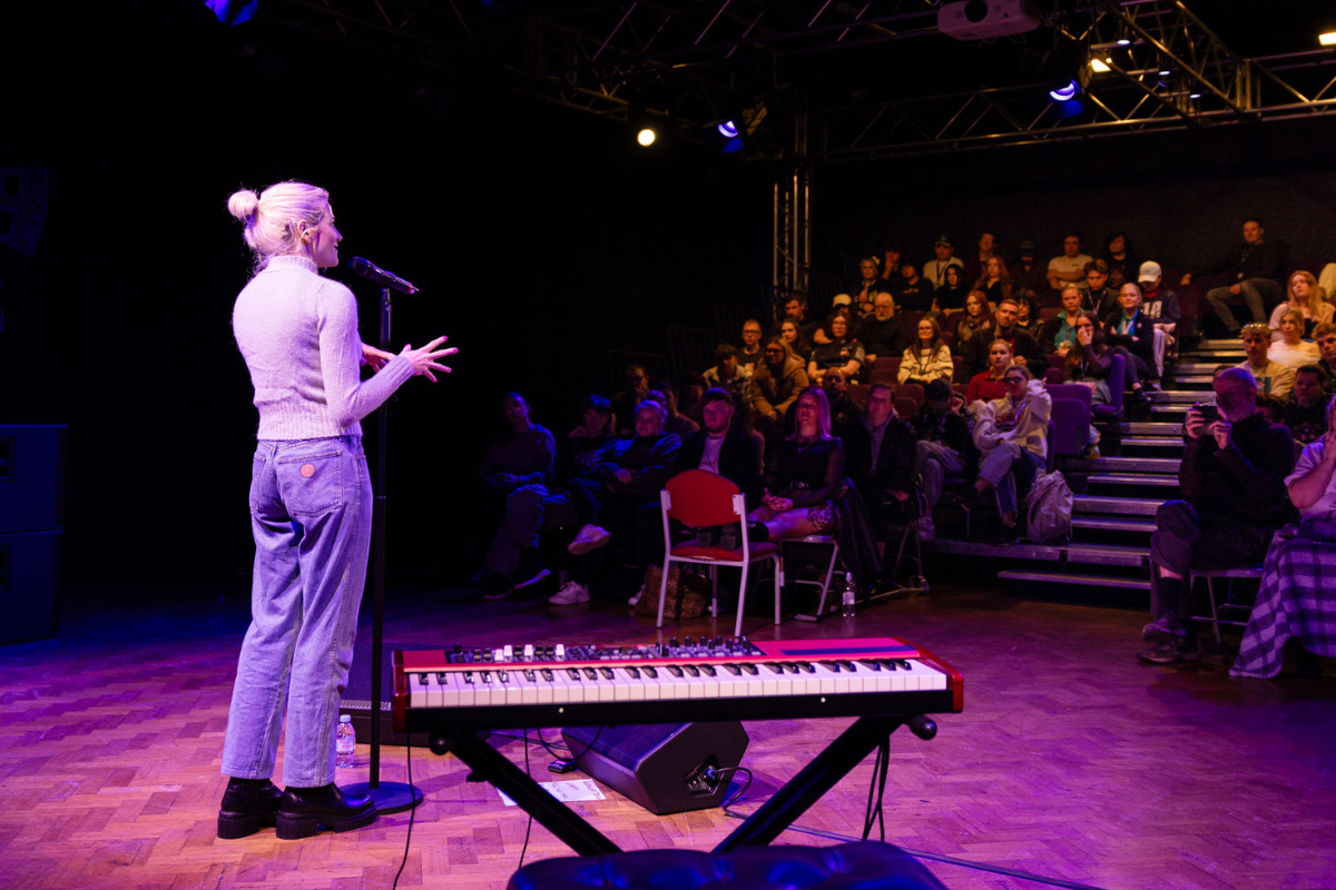Pixie Lott standing at the microphone, taking questions from a crowd of 100 students.