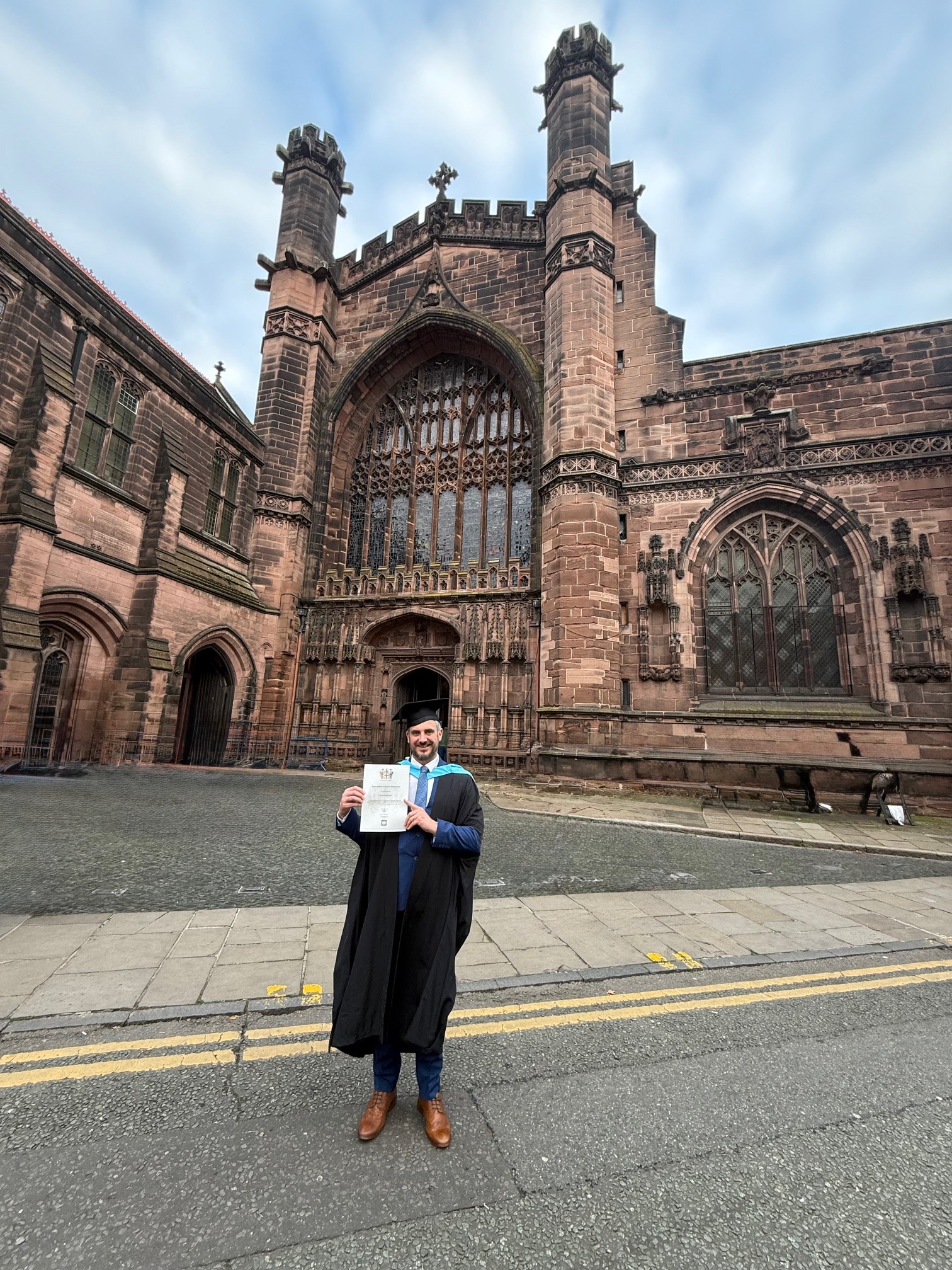 Aaron Brizell in front of Chester Cathedral with his degree.