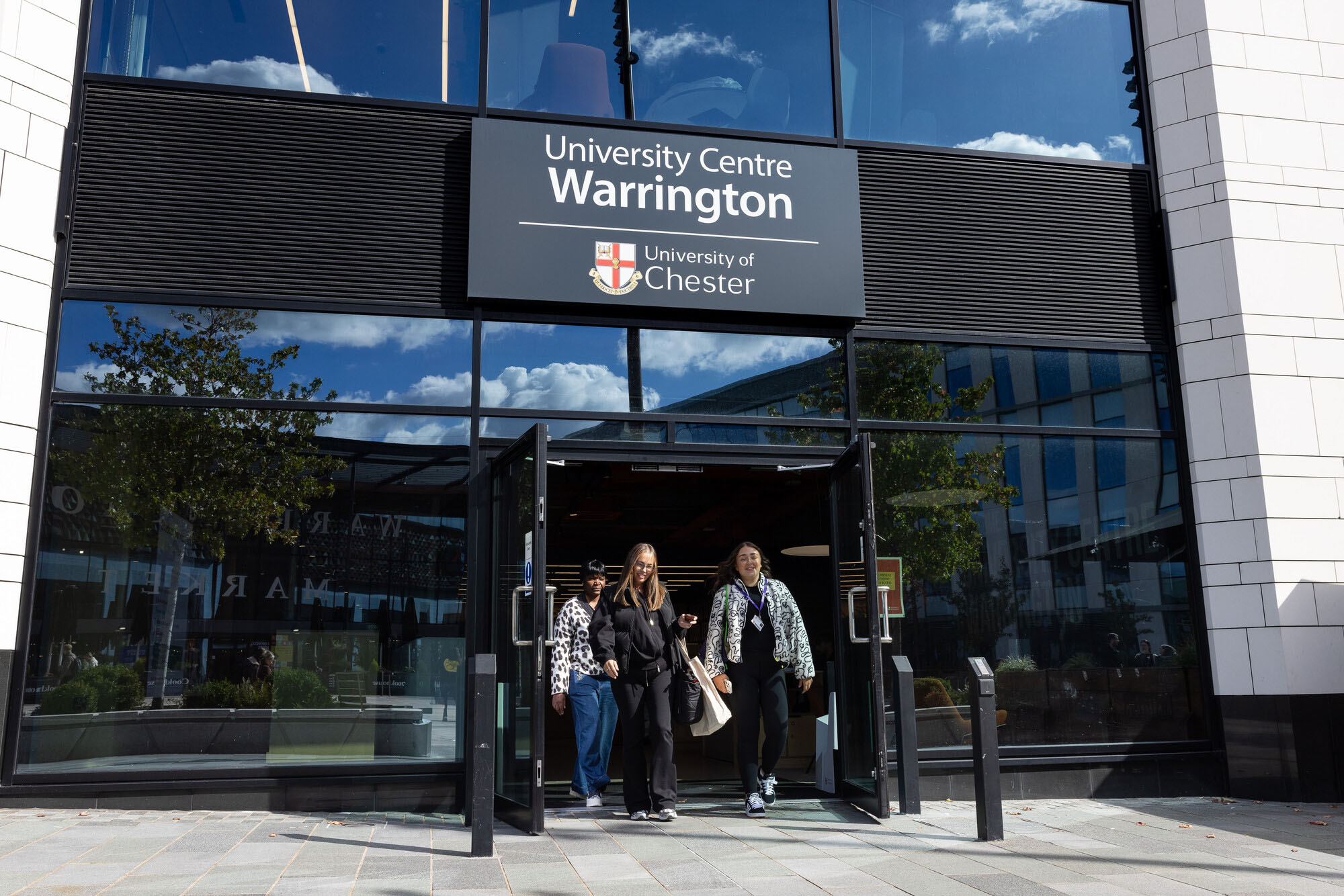 Students leaving the modern glass‑fronted entrance of University Centre Warrington at the University of Chester.