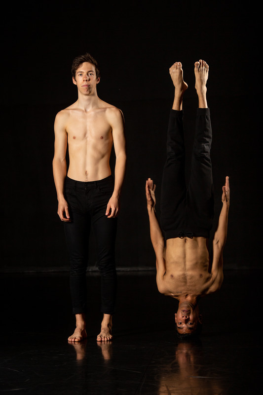 Man executing handstands in a dark space, highlighting elements of a dance course in their degree..