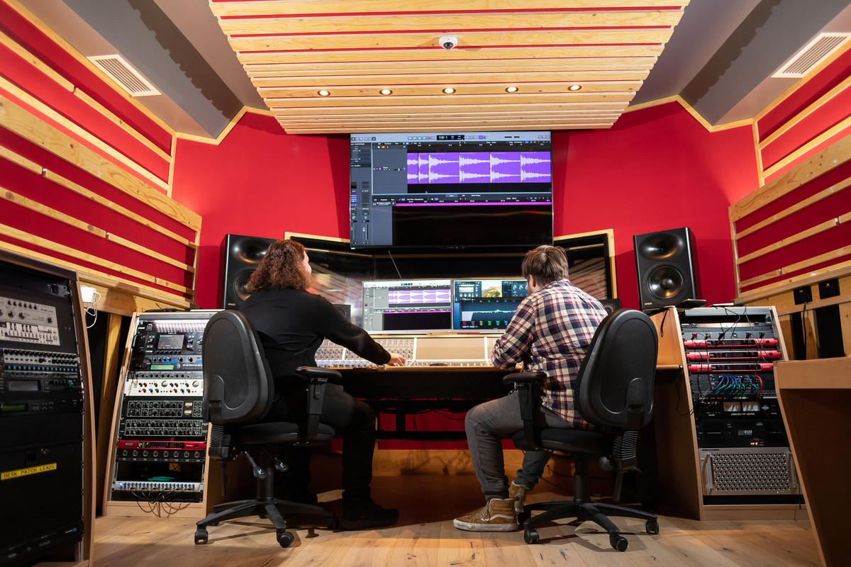 A sound recording studio with two people working at the controls.