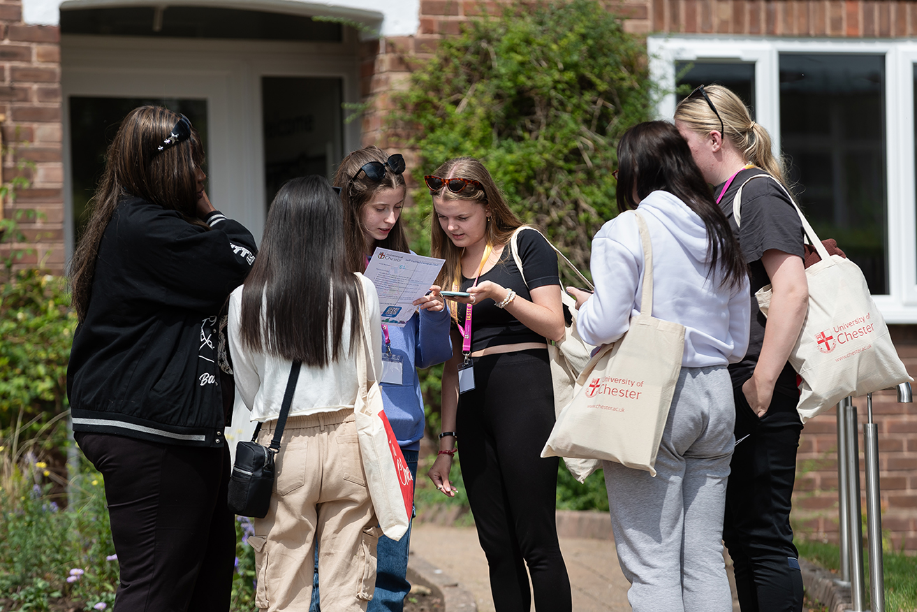Engaged Students outdoors gathered around with a campus map carrying canvas tote bag with 'University of Chester' logo.