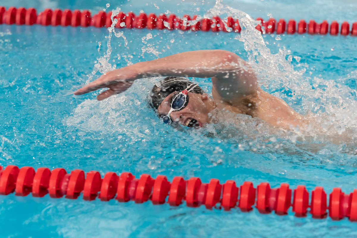 A male student wearing goggles is swimming in the training pool between the red rope lane marker lines.