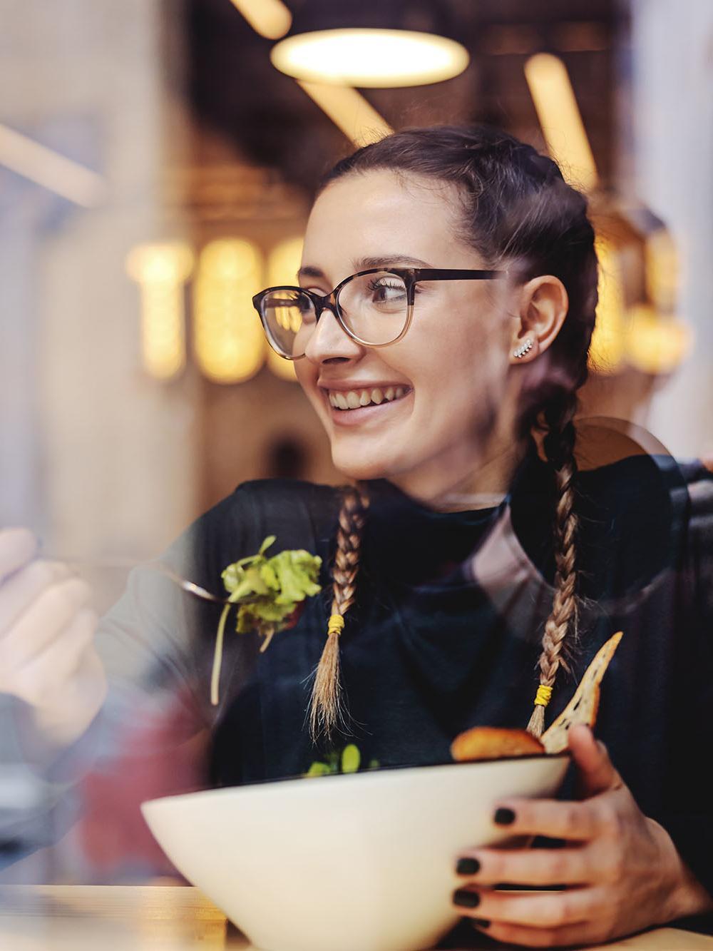 Young smiling girl sitting in restaurant and enjoying her salad for lunch.