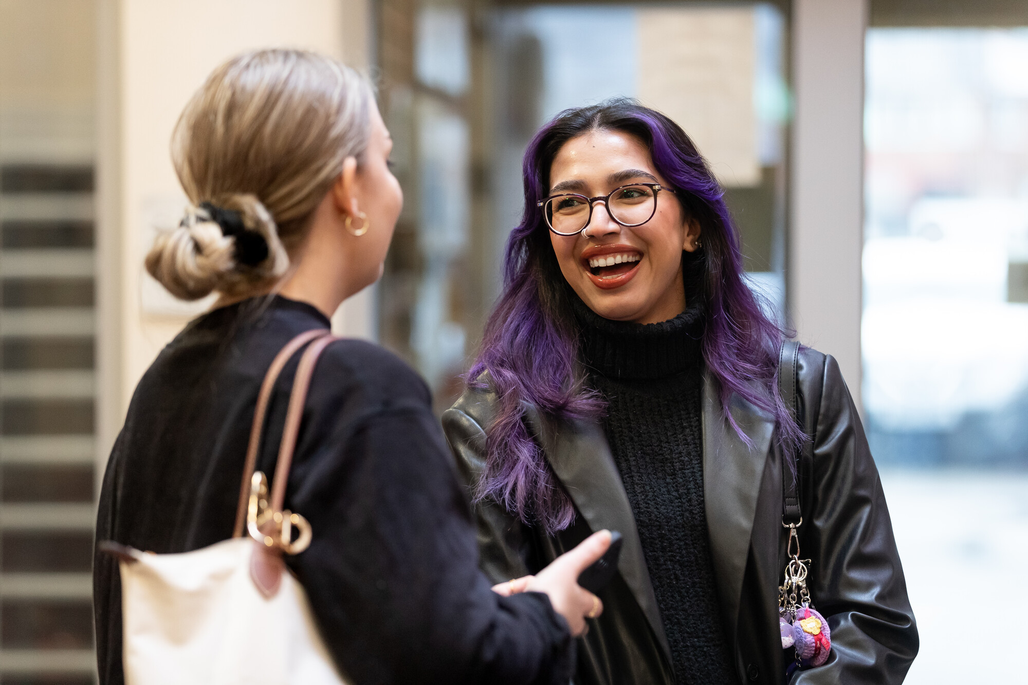Two students smiling and chatting indoors, showcasing the diverse and supportive student community at the university.