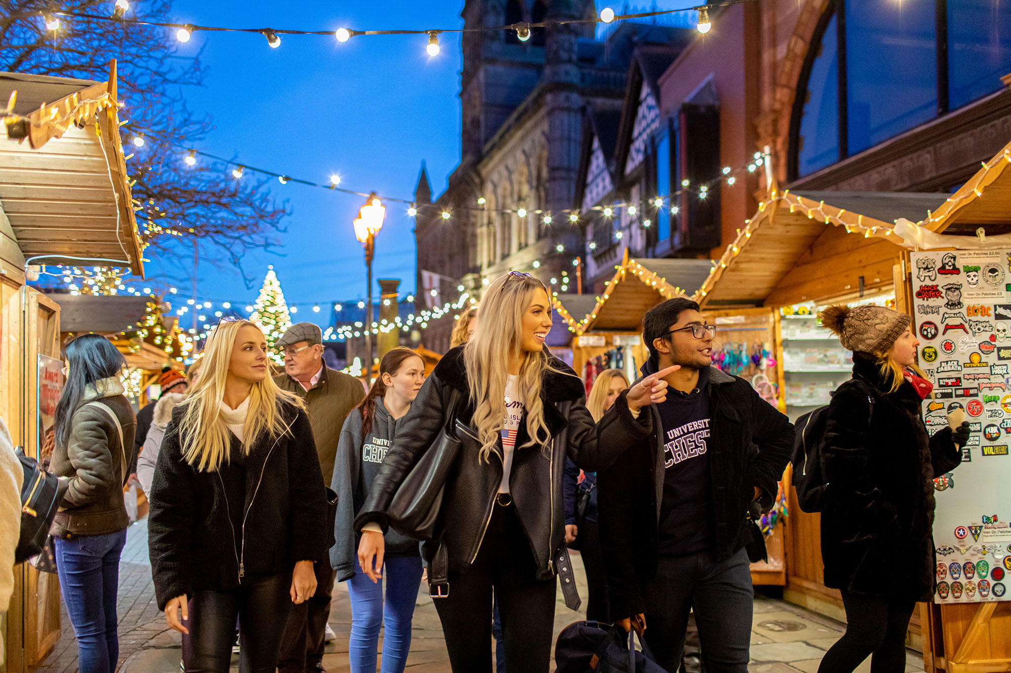 Festive Christmas market with wooden stalls, string lights, and holiday decorations in Chester during the evening.